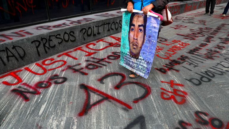 A relative of a missing student holds a poster with his image as she walks past a "+43" sign painted on the ground, during a protest outside the Attorney General&#39;s office, before the sixth anniversary of the disappearance of 43 students of the Ayotzinapa Teacher Training College, in Mexico City, Mexico September 25, 2020. REUTERS/Henry Romero