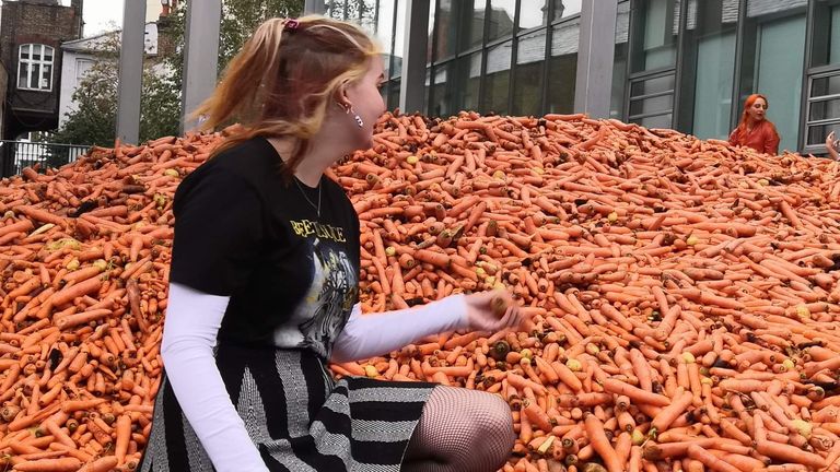 Handout photo courtesy of Josie Power of Eden Groualle next to an art installation of 29 tonnes of carrots dumped outside Goldsmiths College - part of the University of London.
