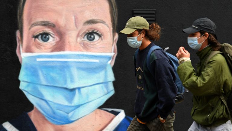 Pedestrians wearing a face mask or covering due to the COVID-19 pandemic, walk past graffiti by the artist @akse_p19, depicting a nurse in scrubs and a face mask, but with an Angel's halo above her head, in Manchester, northwest England on August 3, 2020. - Britain's "Eat out to Help out" scheme began Monday, introduced last month by Chancellor Rishi Sunak to help boost the economy claw its way from a historic decline sparked by the coronavirus crisis. (Photo by Oli SCARFF / AFP) / RESTRICTED TO EDITORIAL USE - MANDATORY MENTION OF THE ARTIST UPON PUBLICATION - TO ILLUSTRATE THE EVENT AS SPECIFIED IN THE CAPTION (Photo by OLI SCARFF/AFP via Getty Images)