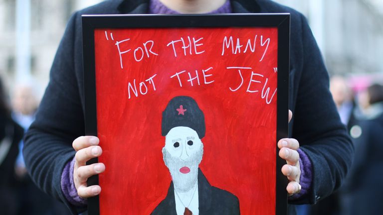 A demonstrator holding a painting saying "For the many not the Jew", as people protest against anti-Semitism in the Labour party in Parliament Square, London, as Jewish community leaders have launched a scathing attack on Jeremy Corbyn, claiming he has sided with anti-Semites "again and again".