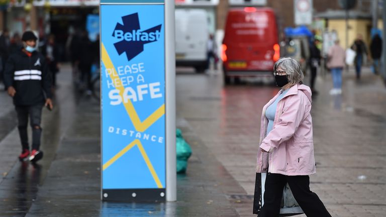 des acheteurs du centre-ville de Belfast portant des masques faciaux passent devant un panneau d'affichage de conseils de santé publique le 14 octobre 2020 à Belfast, en Irlande du Nord. 