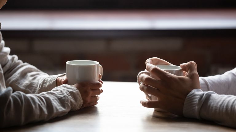 Close up woman and man sitting in cafe, holding warm cups of coffee on table, young couple spending weekend in cozy coffeehouse together, romantic date concept, visitors drinking hot beverages