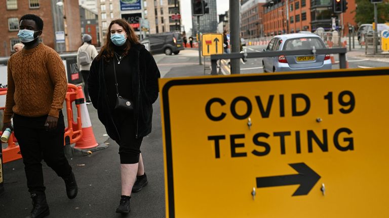 Pedestrians wearing protective face coverings walk past a Covid-19 testing sign in Manchester in north-west England on October 17, 2020, as further restrictions come into force as the number of novel coronavirus COVID-19 cases rises. - About 28 million people in England, more than half the population, are now living under tough restrictions imposed on Saturday as the country battles a surge in coronavirus cases. (Photo by Oli SCARFF / AFP) (Photo by OLI SCARFF/AFP via Getty Images)
