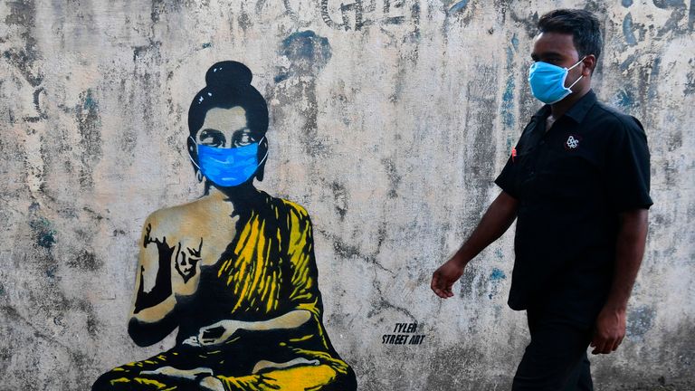 A resident wearing a facemask amid concerns over the spread of the COVID-19 novel coronavirus walks past a graffiti of Buddha wearing facemask, in Mumbai on March 16, 2020. (Photo by INDRANIL MUKHERJEE / AFP) (Photo by INDRANIL MUKHERJEE/AFP via Getty Images)
