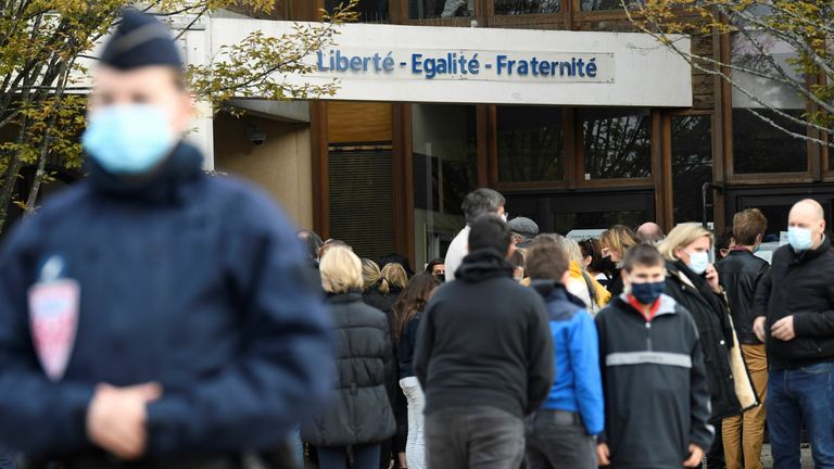المستجيبون للطوارئ (SAMU) يمشون أمام رجال شرطة CRS يقفون أمام مدرسة متوسطة في كونفلانس سانت أونورين ، 30 كم شمال غرب باريس ، في 17 أكتوبر 2020 ، حيث يتم عرض الزهور بعد قطع رأس مدرس من قبل مهاجم أصيب بالرصاص قتلى من قبل رجال الشرطة