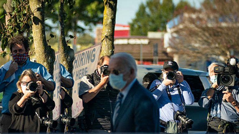 Mr Biden walks past members of the press in a mask