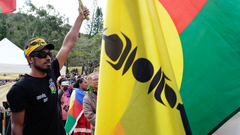 A supporter of independence stands near a flag of the Canaco Socialist National Liberation Front