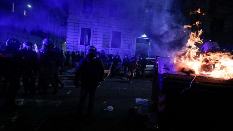 Police officers stand near a burning trash container during a protest over the restrictions put in place to curb the coronavirus disease (COVID-19) infections in Rome, Italy October 27, 2020. REUTERS/Guglielmo Mangiapane