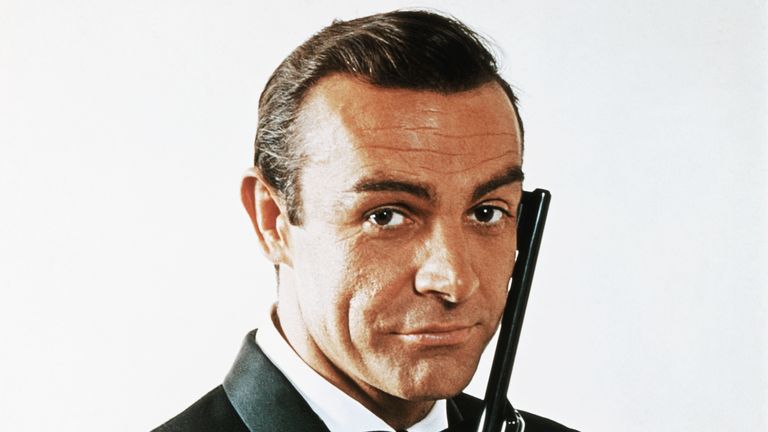 (Original Caption) Waist-up portrait of Sean Connery, as James Bond, caressing the barrel of a gun against the side of his face. Connery is wearing a tuxedo and bow tie and smiling slightly.