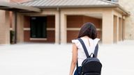 An upset middle school girl hangs her head low while preparing to enter the school building.