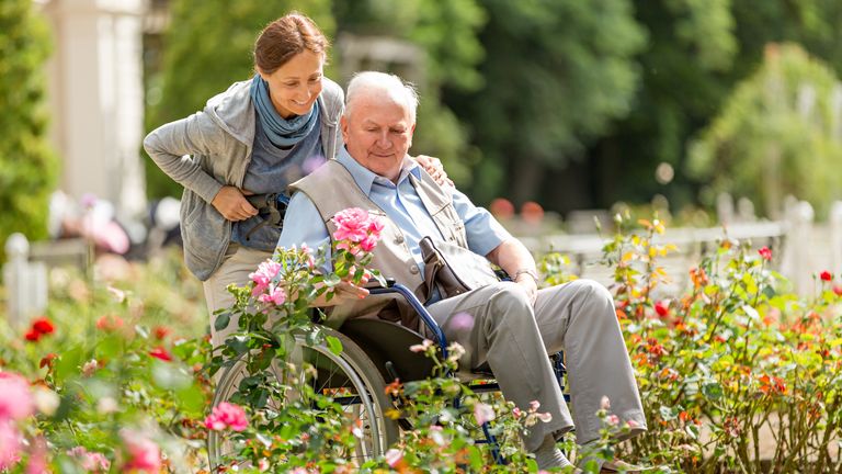 Caregiver and senior man on a wheelchair walking outdoors 