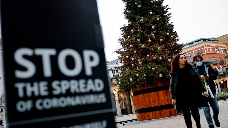 Pedestrians pass a COVID-19 sign reading "Stop the spread" as they walk past a Christmas tree in Covent Garden in central London on November 17, 2020. - Britain has been the worst-hit nation in Europe recording more than 50,000 coronavirus deaths from some 1.2 million positive cases. (Photo by Tolga AKMEN / AFP) (Photo by TOLGA AKMEN/AFP via Getty Images)