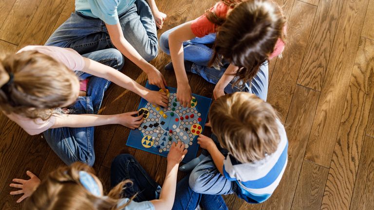 High angle view of a small group of people playing ludu games on the wooden floor at home.