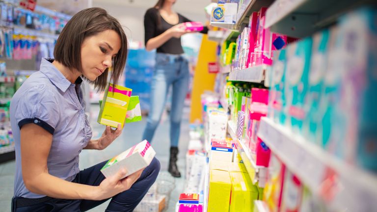 Adult woman crouching and taking time choosing sanitary pads in pharmacy