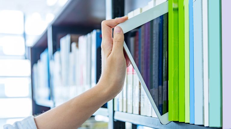 Woman hand choosing tablet from a bookshelf.