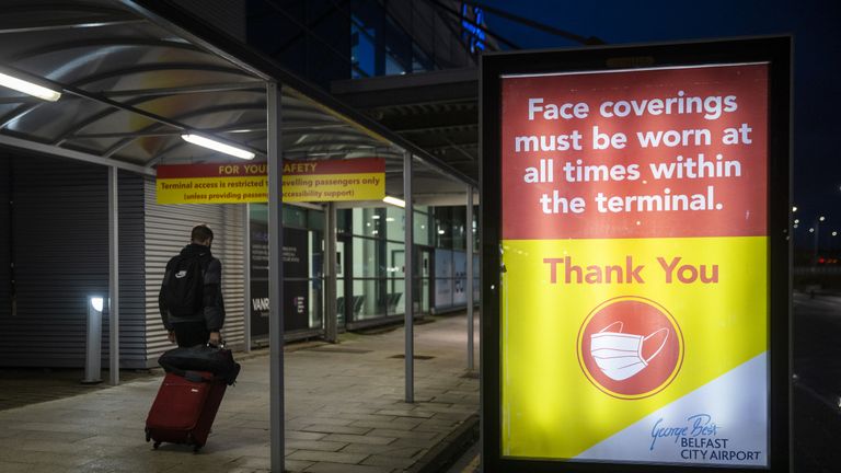 A man pulling luggage walks passed a sign that face coverings must be worn at all times within the terminal at George Best Belfast City Airport. Northern Ireland is considering strengthening its travel locator paperwork and is consulting legal experts after a mutation of coronavirus was discovered in London and Kent.