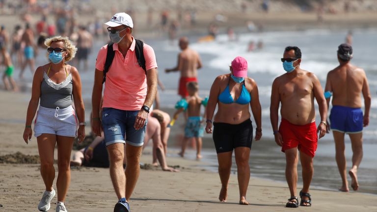 Several people walk along the beach wearing face masks, as the regional government of the Canary Islands forbids smoking without maintaining a safe distance