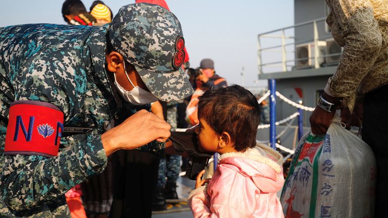 A Bangladesh navy personnel helps a child to wear a mask before getting on board a ship to move to Bhasan Char island in Chattogram