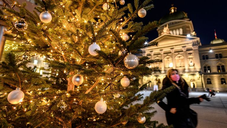 A woman wearing a protective face mask walks past a Christmas tree in front of the Swiss House of Parliament in Bern, Switzerland