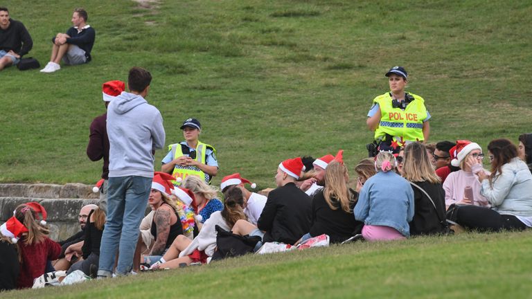 Police officers watch a group of people gathering in a large number breaching public health orders beside Bondi Beach.