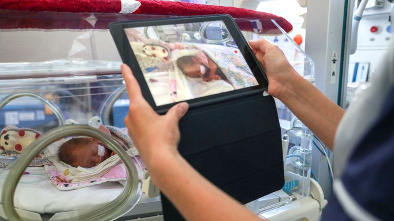 A nurse makes a video of a newborn baby to send to the parents as visiting hours are restricted