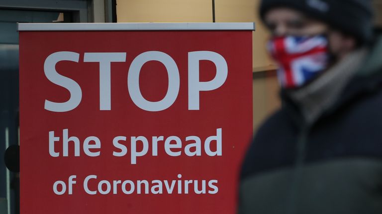 Un hombre con una mascarilla pasa junto a un letrero de advertencia de coronavirus afuera de un banco en Argyle Street en el centro de Glasgow en la mañana después de que se introdujeran medidas de bloqueo más estrictas en Escocia continental.