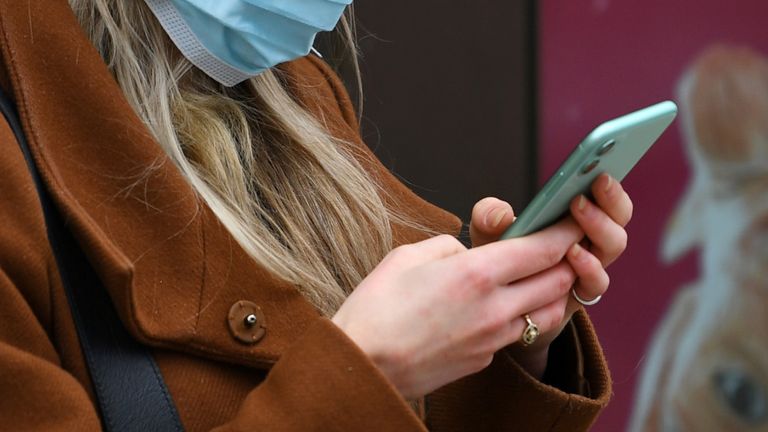 A woman looks at her phone whilst wearing a mask in London