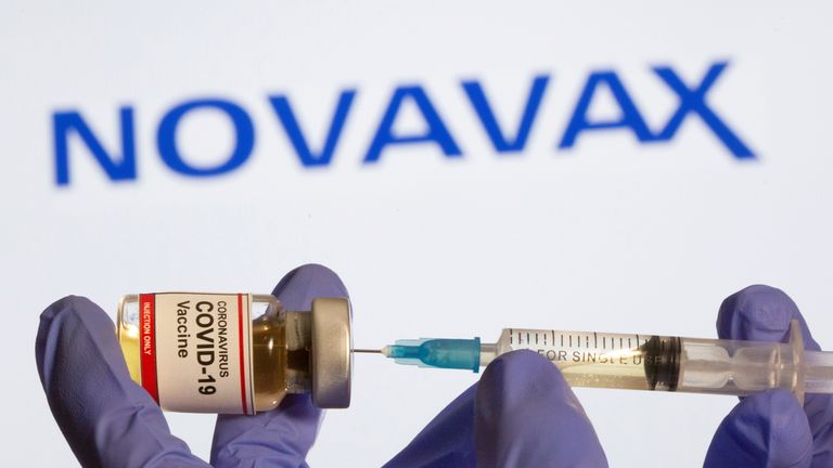 FILE PHOTO: A woman holds a small bottle labeled with a "Coronavirus COVID-19 Vaccine" sticker and a medical syringe in front of displayed Novavax logo in this illustration
