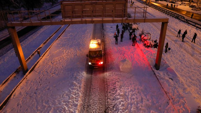 An emergency vehicle drives past people walking in the snow on the M-30 motorway, in Madrid, Spain, January 9, 2021. REUTERS/Susana Vera
