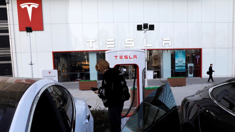 A woman charges a Tesla car in front of the electric vehicle maker's showroom in Beijing, China January 5, 2021