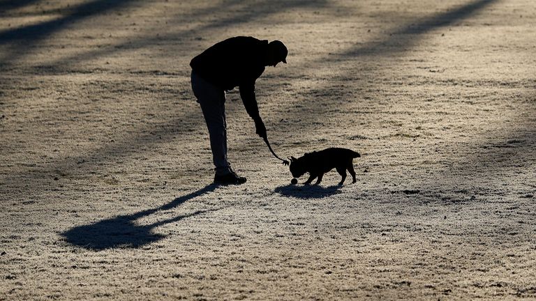 A man plays with his dog on the frozen lawn in a park in London.