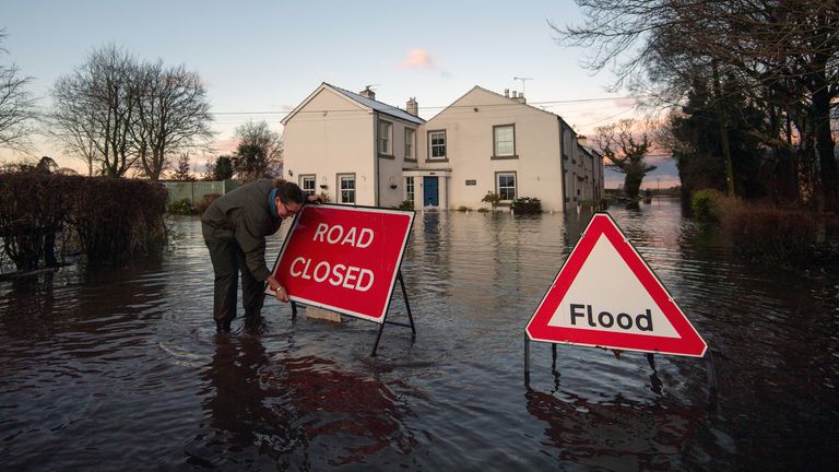 Gabrielle Burns-Smith erects a road closed sign on Warrington Lane on the outskirts of Lymm in Cheshire as Storm Christoph causes widespread flooding across the UK. Picture date: Thursday January 21, 2021.