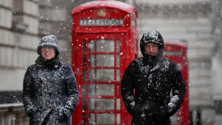 People walk through central London, as snow falls