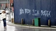 A woman walks past graffiti saying &#39;No Irish Sea Border&#39; in Belfast city centre, Northern Ireland