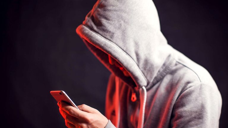 Man wearing hoody sweater with mobile phone in hands. Crime and hacking concept