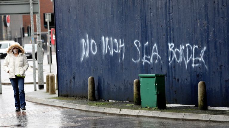 زنی از کنار دیوار نویسی عبور می کند و می گوید & # 39؛ بدون مرز دریایی ایرلند & # 39؛  در مرکز شهر بلفاست ، ایرلند شمالی