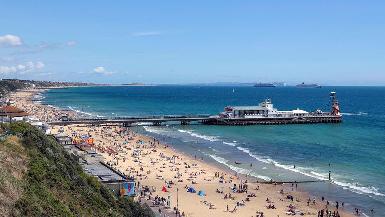 Cruise ships pass by as people enjoy the beach at Bournemouth as the hot weather continues.