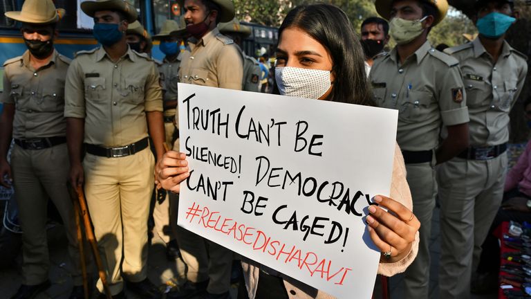 A protester holds a sign in support of Ms Ravi next to a line of police officers in Bengaluru