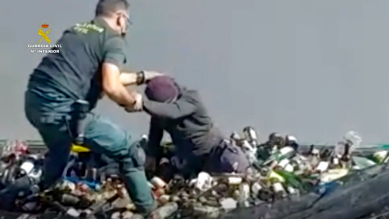 Ein Beamter der Zivilgarde hilft einem Mann, unter Glasflaschen in einen Container in Melilla zu gelangen.  Bild: AP