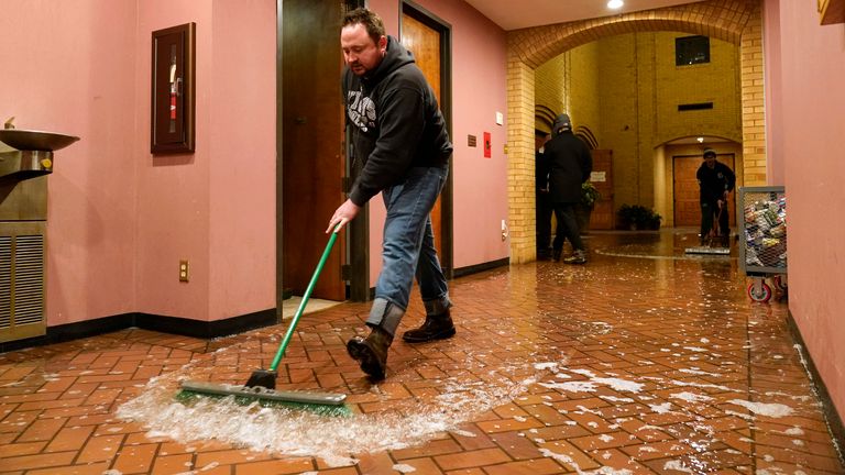 Father John Szatkowski of St. Paul The Apostle Church sweeps water from a broken water line out of his church in Richardson, Texas, Wednesday, Feb. 17, 2021.  (AP Photo/Tony Gutierrez)