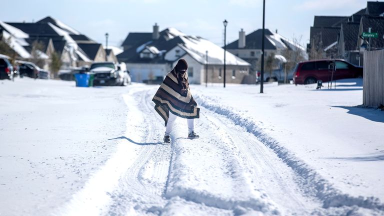 A man walks to his friend&#39;s home in a neighbourhood without electricity as snow covers the BlackHawk neighborhood in Pflugerville