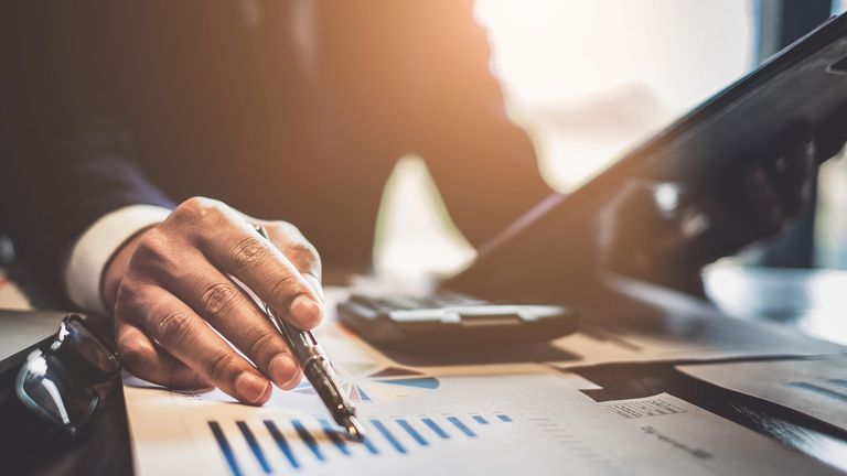 Close up Businessman consultant holding pen and pointing at financial on wooden desk in coffee shop. freelance, tax, accounting, statistics and analytic research concept.