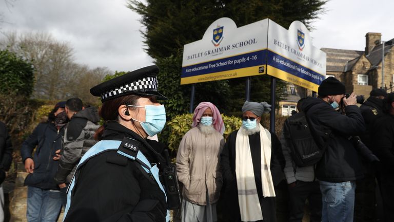 Un policier observe des manifestants rassemblés devant le Batley Grammar School de Batley, dans le West Yorkshire, où un enseignant a été suspendu pour avoir montré une caricature du prophète Mahomet à des élèves lors d'un cours d'études religieuses.  Date de la photo: vendredi 26 mars 2021.