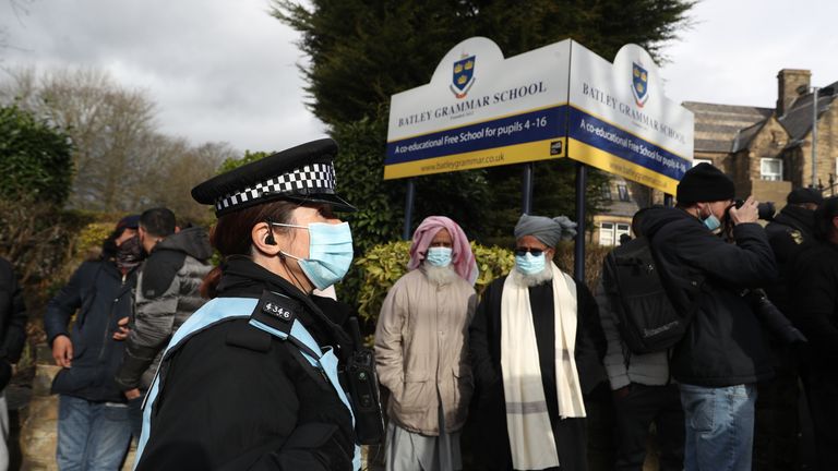 A police officer observes protesters gathered outside Batley Grammar School in Batley, West Yorkshire, where a teacher has been suspended for reportedly showing a caricature of the Prophet Mohammed to pupils during a religious studies lesson. Picture date: Friday March 26, 2021.