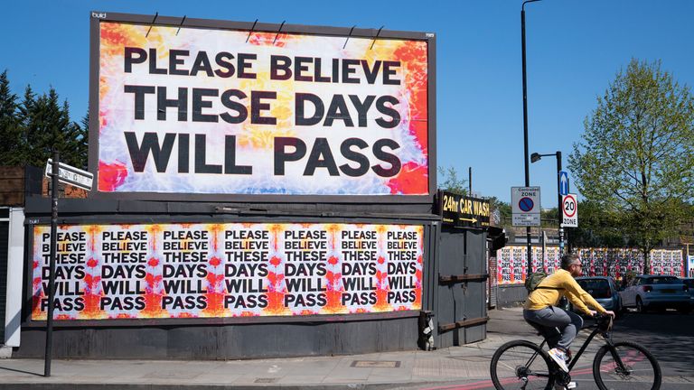 A cyclist rides past a billboard reading &#39;please believe these days will pass&#39; in Shoreditch, east London, as the UK continues in lockdown to help curb the spread of the coronavirus.