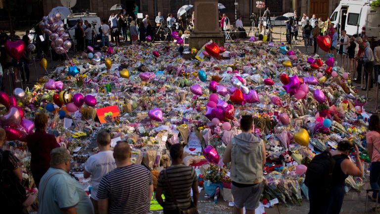 People stand next to flowers for the victims of Monday's bombing at St Ann's Square in central Manchester, England, Friday, May 26 2017. British police investigating the Manchester Arena bombing arrested a ninth man while continuing to search addresses associated with the bomber. (AP Photo/Emilio Morenatti) 