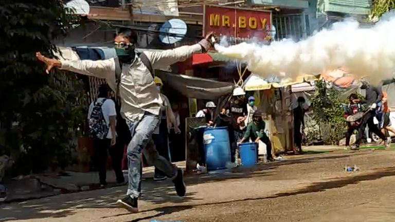 A demonstrator runs with a tear gas canister during a protest in Yangon