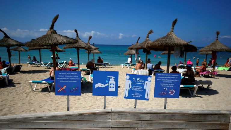 Signs are pictured as people sunbathe and swim on El Arenal beach in Palma de Mallorca (file pic)