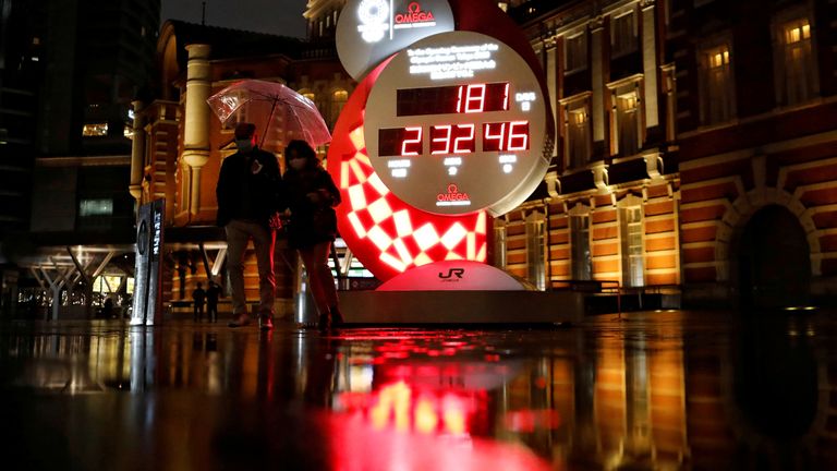 Passersby walk past a countdown clock to the Games