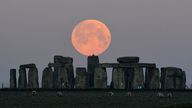 Sheep graze as the full moon, known as the "Super Pink Moon", sets behind Stonehenge stone circle near Amesbury, Britain, April 27, 2021. REUTERS/Toby Melville